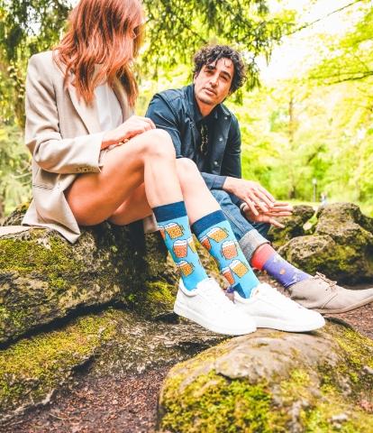 Mann und Frau sitzen auf einem Felsen und tragen bunte Socken (Cheers Beers bzw. Biergläser-Motiv)